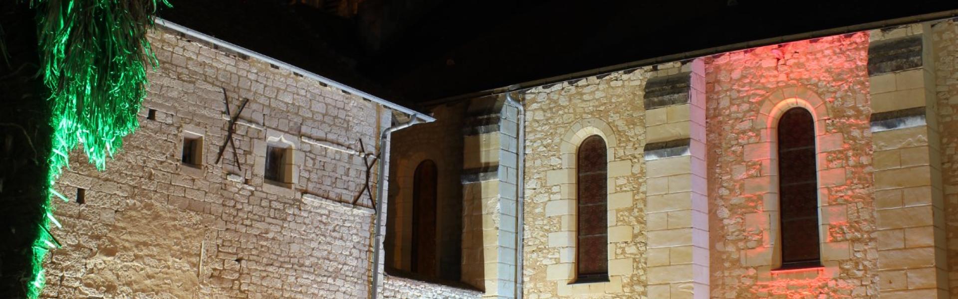 Une photo de nuit à l'extérieur du Prieuré Saint-André éclairé. Le public écoute les musiciens à côté d'un palmier.