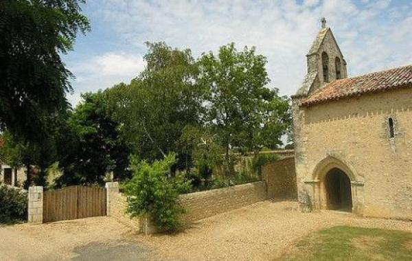 Une vue en journée de l'entrée de la Chapelle de Cramard avec de la verdure et un ciel bleu et nuageux.