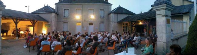 Une photo en fin de journée de la cour de la Mairie de Frozes. Un public très nombreux écoute les musiciens.