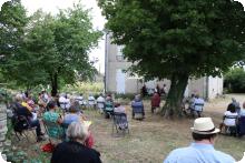 Une photo d'un concert à la Maison Tassin. Du public assis en plein air écoute des musiciens.