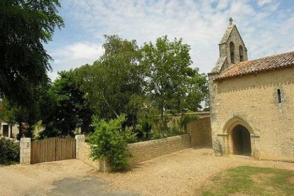 Une vue en journée de l'entrée de la Chapelle de Cramard avec de la verdure et un ciel bleu et nuageux.